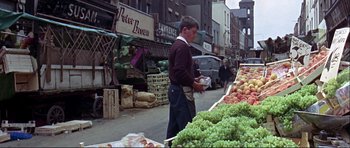 Movie still from “Alfie” (1966), directed by Lewis Gilbert – A man standing in front of an outdoor fruit stand; Wide shot, High angle