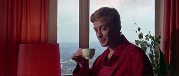 Movie still from “Alfie” (1966), directed by Lewis Gilbert – A man holding a coffee cup while sitting in front of a window; Medium shot, Low angle