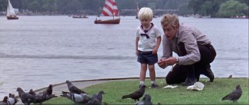Movie still from “Alfie” (1966), directed by Lewis Gilbert – A man and a child looking at pigeons on the grass; Medium shot, High angle
