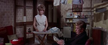 Movie still from “Alfie” (1966), directed by Lewis Gilbert – A woman standing in front of an ironing board in front of a man; Medium shot, High angle