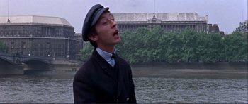 Movie still from “Alfie” (1966), directed by Lewis Gilbert – A man in a hat and a jacket standing in front of a body of water; Close Up shot, Low angle