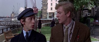 Movie still from “Alfie” (1966), directed by Lewis Gilbert – Two men in suits and hats are standing in a park; Medium shot, Over the shoulder angle