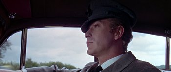 Movie still from “Alfie” (1966), directed by Lewis Gilbert – A man wearing a hat sitting in the driver's seat of a car; Close Up shot, Low angle