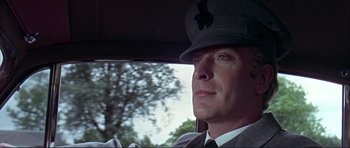 Movie still from “Alfie” (1966), directed by Lewis Gilbert – A man wearing a hat sitting in the driver's seat of a car; Close Up shot, Low angle