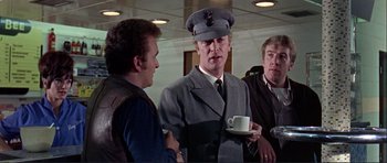 Movie still from “Alfie” (1966), directed by Lewis Gilbert – A man wearing a hat and holding a cup of coffee; Medium shot, Over the shoulder angle