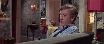 Movie still from “Alfie” (1966), directed by Lewis Gilbert – A man sitting on a couch holding up a glass of beer; Medium shot, Over the shoulder angle