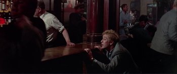 Movie still from “Alfie” (1966), directed by Lewis Gilbert – A man sitting at a table in front of other people; Medium shot, Over the shoulder angle