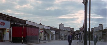 Movie still from “Alfie” (1966), directed by Lewis Gilbert – A man in a suit and tie standing on the sidewalk; Extreme Wide shot, Low angle