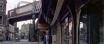 Movie still from “Alfie” (1966), directed by Lewis Gilbert – A man in a suit and tie standing on a sidewalk; Wide shot, Low angle
