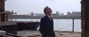 Movie still from “Alfie” (1966), directed by Lewis Gilbert – A man standing on a beach near a body of water; Medium shot, Low angle