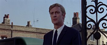 Movie still from “Alfie” (1966), directed by Lewis Gilbert – A man wearing a suit and tie standing in front of a building; Close Up shot, Low angle