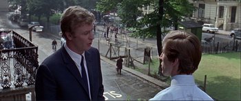 Movie still from “Alfie” (1966), directed by Lewis Gilbert – Two men in suits talking on the sidewalk; Medium shot, Over the shoulder angle