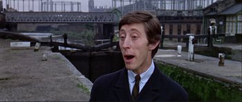 Movie still from “Alfie” (1966), directed by Lewis Gilbert – A man in a suit and tie standing in front of a river; Close Up shot, Low angle