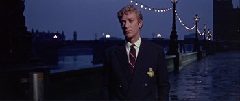 Movie still from “Alfie” (1966), directed by Lewis Gilbert – A man in a suit and tie standing on a bridge; Medium shot, Low angle