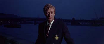 Movie still from “Alfie” (1966), directed by Lewis Gilbert – A man wearing a suit and tie standing in front of a body of water; Close Up shot, Low angle