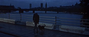 Movie still from “Alfie” (1966), directed by Lewis Gilbert – A person walking a dog on a sidewalk near a body of water; Wide shot, Low angle