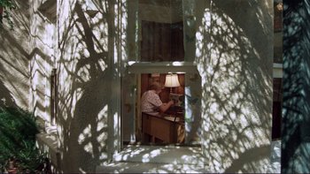 Movie still from “Alice Doesn't Live Here Anymore” (1974), directed by Martin Scorsese – An older man sitting at a desk in a room with a lamp; Wide shot, Low angle