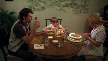Movie still from “Alice Doesn't Live Here Anymore” (1974), directed by Martin Scorsese – A man and a boy sitting at a wooden table eating cake; Medium shot, High angle