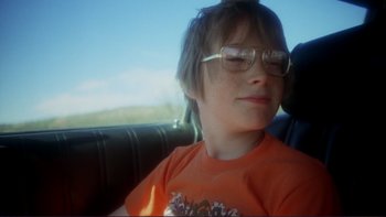 Movie still from “Alice Doesn't Live Here Anymore” (1974), directed by Martin Scorsese – A young boy wearing glasses sitting in the back seat of a car; Close Up shot, Low angle