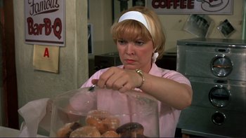 Movie still from “Alice Doesn't Live Here Anymore” (1974), directed by Martin Scorsese – A woman in a pink shirt and white headband holding a container of donuts; Close Up shot, Over the shoulder angle
