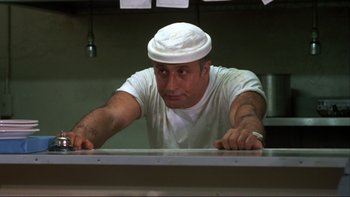 Movie still from “Alice Doesn't Live Here Anymore” (1974), directed by Martin Scorsese – A man wearing a white hat is leaning over a counter; Medium shot, Low angle