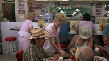 Movie still from “Alice Doesn't Live Here Anymore” (1974), directed by Martin Scorsese – A group of people sitting at a table in front of a counter; Wide shot, Over the shoulder angle