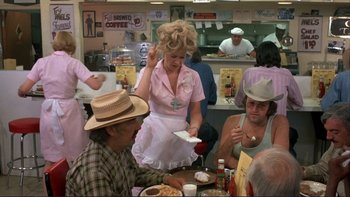Movie still from “Alice Doesn't Live Here Anymore” (1974), directed by Martin Scorsese – A woman in a waitress uniform is serving a customer; Medium shot, Over the shoulder angle