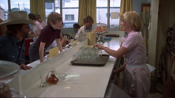 Movie still from “Alice Doesn't Live Here Anymore” (1974), directed by Martin Scorsese – A group of people sitting at a table with glasses on it; Medium shot, Over the shoulder angle