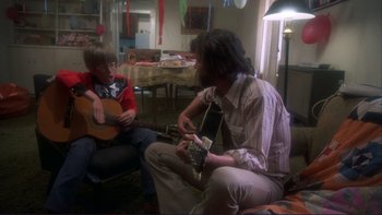 Movie still from “Alice Doesn't Live Here Anymore” (1974), directed by Martin Scorsese – A man and a boy are playing a guitar together; Medium shot, Over the shoulder angle