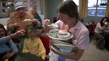 Movie still from “Alice Doesn't Live Here Anymore” (1974), directed by Martin Scorsese – A woman holding a stack of plates and cups; Medium shot, Low angle