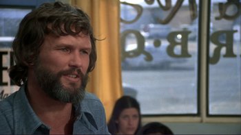 Movie still from “Alice Doesn't Live Here Anymore” (1974), directed by Martin Scorsese – A man with a beard is sitting in front of other people; Close Up shot, Over the shoulder angle