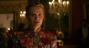 Movie still from “Alice Through the Looking Glass” (2016), directed by James Bobin – A woman in a colorful dress standing in front of chandeliers; Close Up shot, Over the shoulder angle