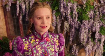 Movie still from “Alice Through the Looking Glass” (2016), directed by James Bobin – A young girl in a purple floral dress standing in front of a wall of purple flowers; Close Up shot, Over the shoulder angle