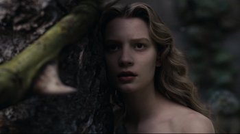 Movie still from “Alice in Wonderland” (2010), directed by Tim Burton – A woman with long blonde hair is standing next to a tree; Close Up shot, Low angle