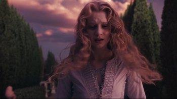 Movie still from “Alice in Wonderland” (2010), directed by Tim Burton – A woman with long blonde hair standing in front of trees; Medium shot, Low angle