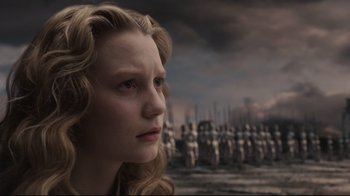 Movie still from “Alice in Wonderland” (2010), directed by Tim Burton – A young woman is looking into the distance while standing in front of statues; Close Up shot, Low angle