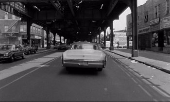 Movie still from “Alice in the Cities” (1974), directed by Wim Wenders – A car driving down a street under an underpass; Wide shot, Low angle