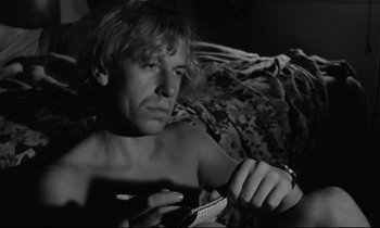 Movie still from “Alice in the Cities” (1974), directed by Wim Wenders – A man sitting on a bed holding a notebook; Close Up shot, Low angle