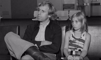 Movie still from “Alice in the Cities” (1974), directed by Wim Wenders – A man sitting next to a young girl in a chair; Medium shot, Low angle