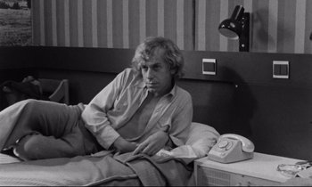 Movie still from “Alice in the Cities” (1974), directed by Wim Wenders – Black and white photograph of a man sitting on a bed; Medium shot, High angle