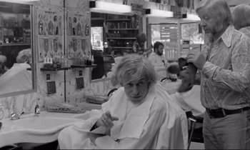 Movie still from “Alice in the Cities” (1974), directed by Wim Wenders – A woman sitting in a chair in front of a bunch of people; Medium shot, Over the shoulder angle
