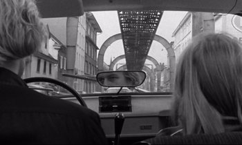 Movie still from “Alice in the Cities” (1974), directed by Wim Wenders – A black and white photo of a woman in the rear view mirror of a car; Wide shot, Over the shoulder angle