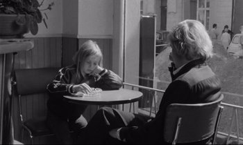 Movie still from “Alice in the Cities” (1974), directed by Wim Wenders – Two people sitting at a table in front of each other; Medium shot, Over the shoulder angle