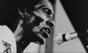 Movie still from “Alice in the Cities” (1974), directed by Wim Wenders – A black - and - white photo of a man speaking into a microphone; Extreme Close Up shot, Low angle
