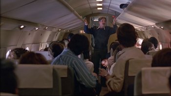 Movie still from “Alive” (1993), directed by Frank Marshall – A man in a black shirt is on a plane; Medium shot, Low angle