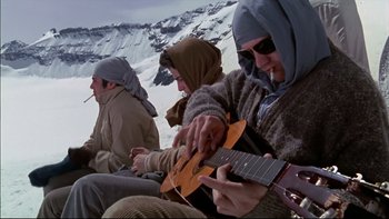 Movie still from “Alive” (1993), directed by Frank Marshall – A group of men sitting on a hill playing a guitar; Wide shot, Low angle