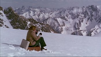 Movie still from “Alive” (1993), directed by Frank Marshall – A woman sitting on a suitcase on top of a snow covered slope; Wide shot, High angle