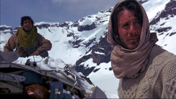 Movie still from “Alive” (1993), directed by Frank Marshall – A man in a scarf standing on top of a snow covered slope; Medium shot, Low angle