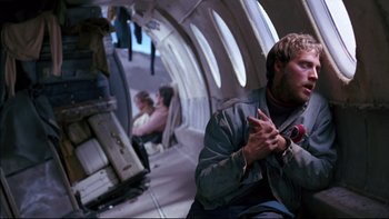 Movie still from “Alive” (1993), directed by Frank Marshall – A man sitting in an airplane holding a microphone; Medium shot, Over the shoulder angle