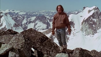 Movie still from “Alive” (1993), directed by Frank Marshall – A man standing on top of a mountain with snow covered mountains in the background; Wide shot, Low angle